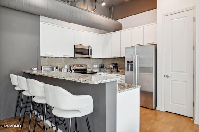 kitchen with white cabinets, decorative backsplash, light hardwood / wood-style floors, light stone counters, and stainless steel appliances