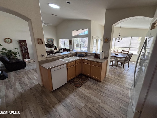 kitchen with stainless steel refrigerator, lofted ceiling, sink, white dishwasher, and kitchen peninsula