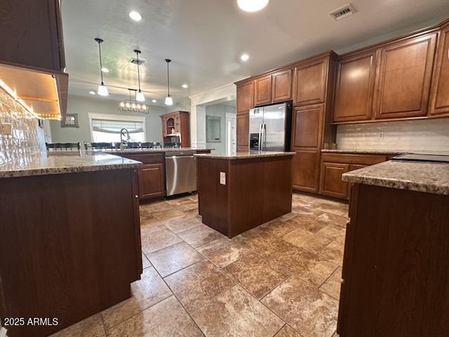 kitchen featuring stone counters, stainless steel appliances, a center island, and tasteful backsplash
