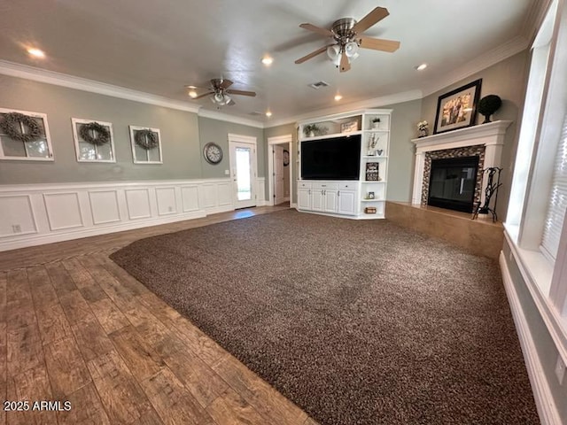 unfurnished living room with a fireplace, crown molding, a ceiling fan, and wainscoting