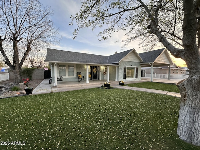 back of house featuring a porch, a shingled roof, fence, and a lawn