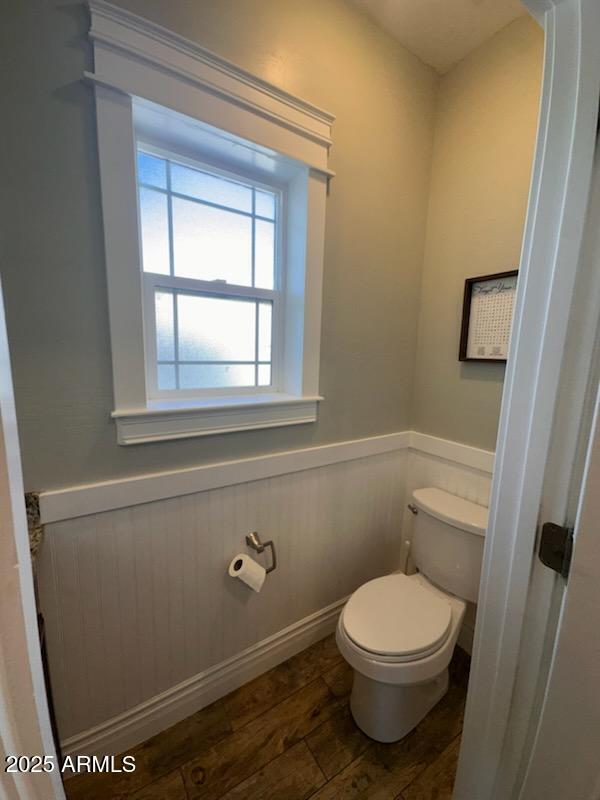 bathroom featuring a wainscoted wall, toilet, and wood finished floors