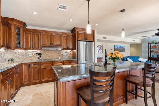 kitchen with high end refrigerator, a kitchen bar, ceiling fan, and an island with sink