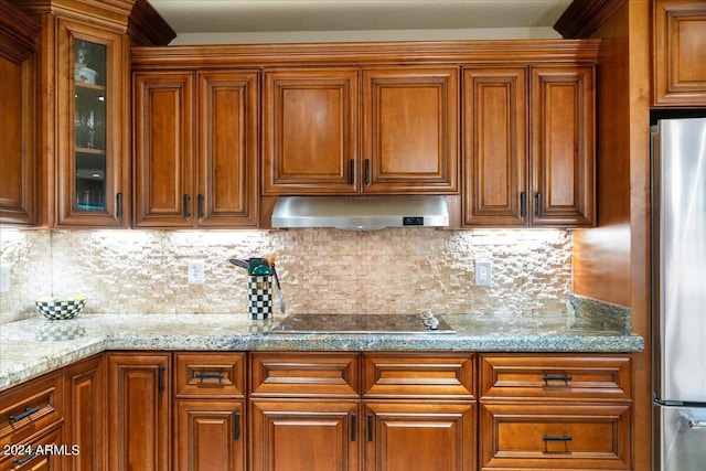 kitchen featuring decorative backsplash, light stone counters, black electric cooktop, and stainless steel fridge