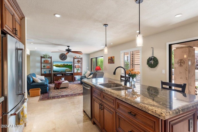 kitchen with ceiling fan, hanging light fixtures, sink, a center island with sink, and stainless steel appliances