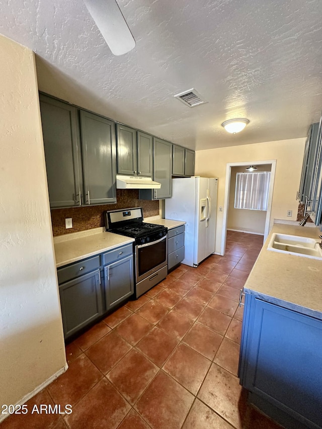 3211 W Campbell Ave, Phoenix, AZ 85017 - kitchen with stainless steel gas range, white refrigerator with ice dispenser, under cabinet range hood, dark tile patterned flooring, and a textured ceiling