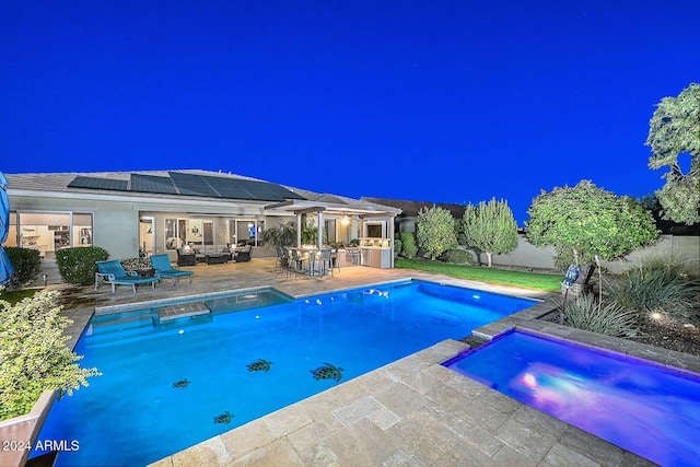 pool at night with an in ground hot tub, an outdoor living space, area for grilling, and a patio area