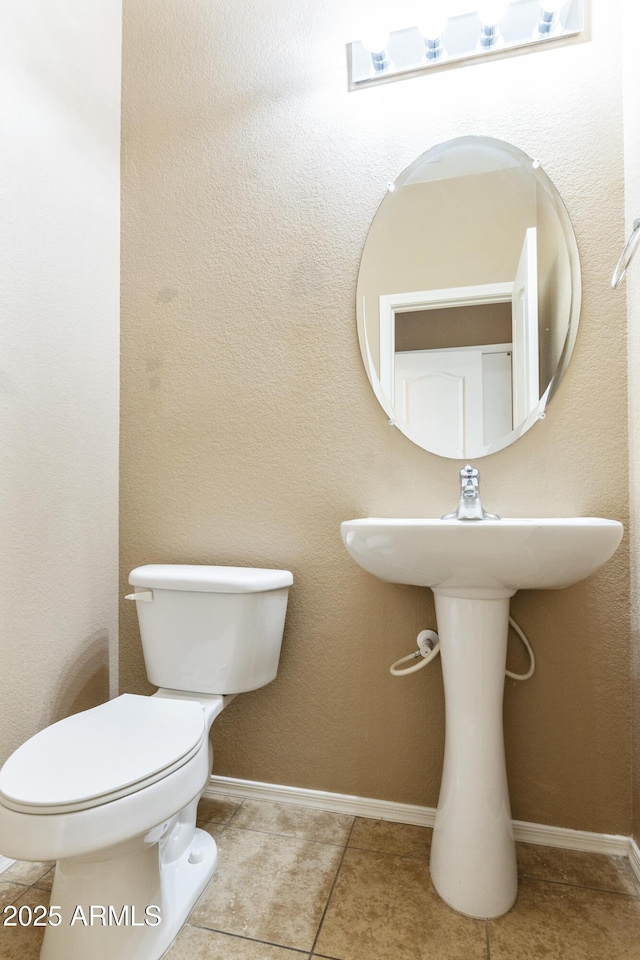 half bath featuring tile patterned floors, toilet, and baseboards