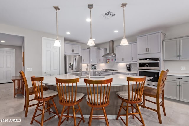 kitchen with an island with sink, a breakfast bar, wall chimney exhaust hood, and stainless steel appliances