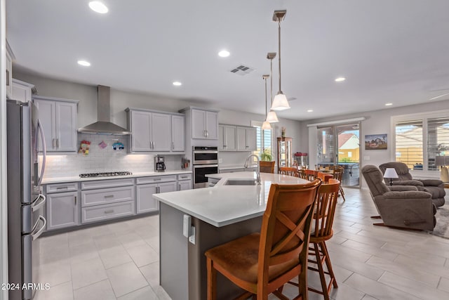 kitchen with pendant lighting, sink, wall chimney exhaust hood, appliances with stainless steel finishes, and a breakfast bar area