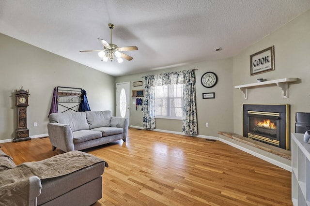 living room featuring a ceiling fan, baseboards, light wood finished floors, lofted ceiling, and a glass covered fireplace