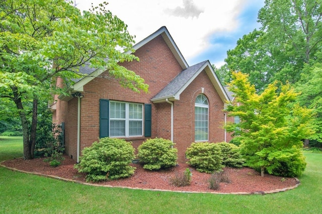 view of home's exterior featuring a shingled roof, a lawn, and brick siding