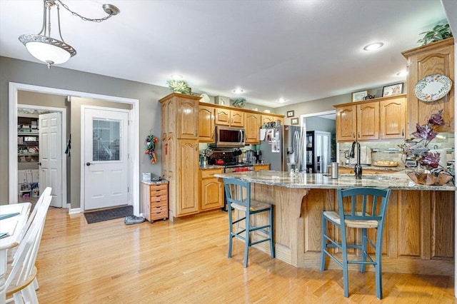 kitchen with stainless steel appliances, tasteful backsplash, light stone countertops, light wood-type flooring, and a kitchen bar