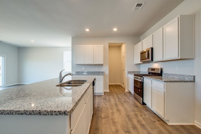 kitchen featuring light stone counters, appliances with stainless steel finishes, white cabinets, a sink, and an island with sink