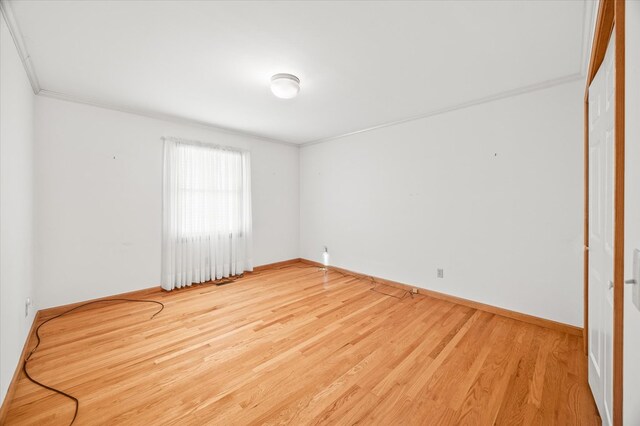 empty room with crown molding, wood finished floors, and baseboards