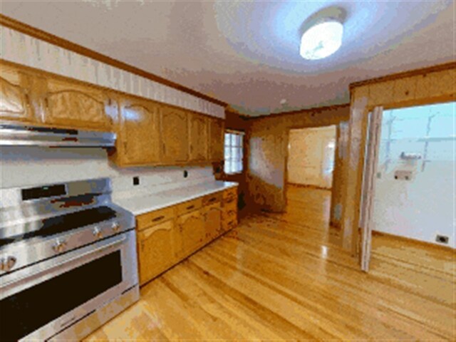 kitchen with light wood-style floors, brown cabinets, ventilation hood, light countertops, and stainless steel range oven