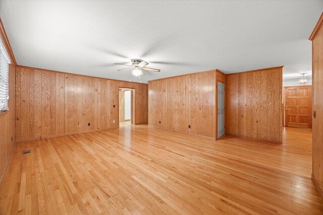 spare room featuring light wood finished floors, visible vents, a ceiling fan, and wood walls