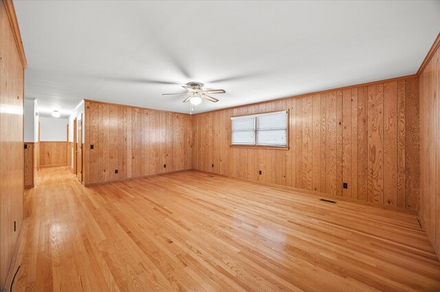 unfurnished room featuring ceiling fan, light wood finished floors, wood walls, and visible vents