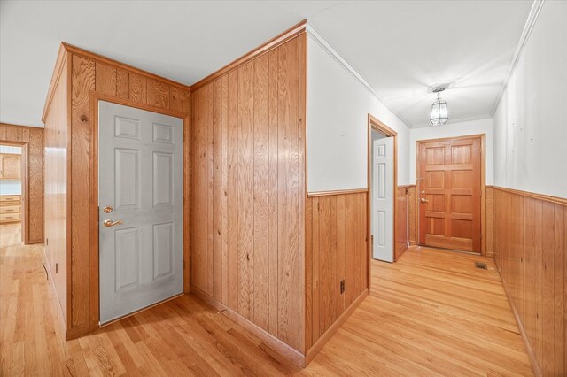 corridor with light wood-style floors, wooden walls, crown molding, and a wainscoted wall