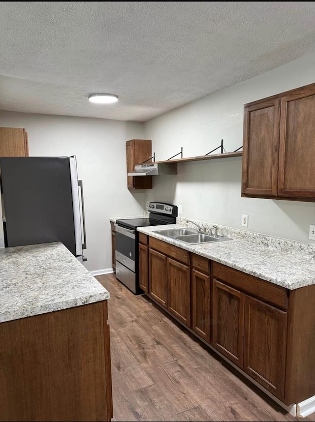 kitchen with a sink, open shelves, wood finished floors, appliances with stainless steel finishes, and light countertops