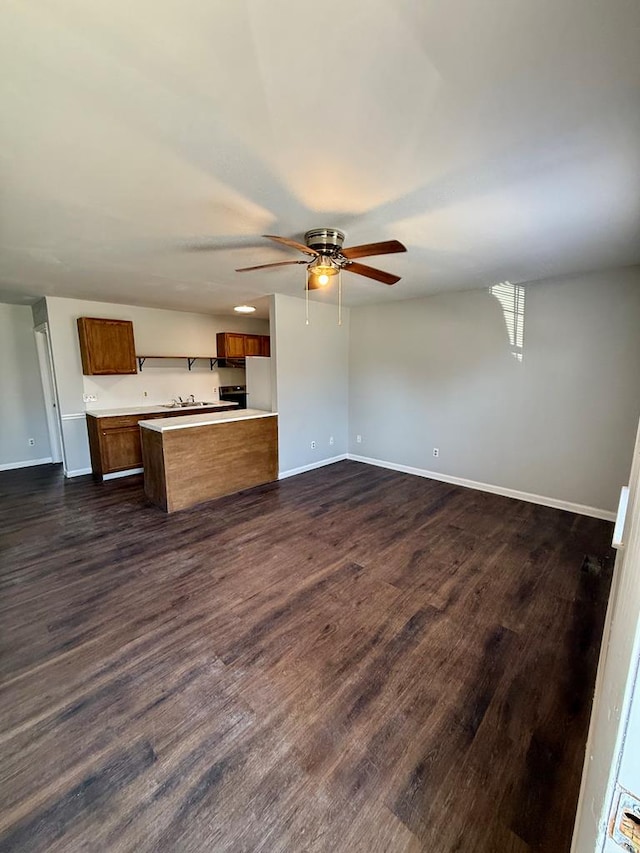 kitchen featuring baseboards, brown cabinets, dark wood finished floors, light countertops, and open floor plan