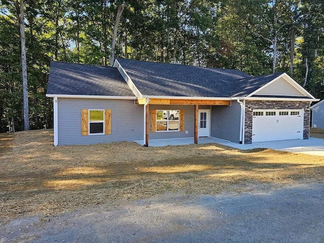 ranch-style house featuring a shingled roof, covered porch, concrete driveway, a garage, and stone siding