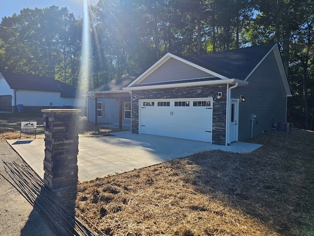 ranch-style home featuring a garage, stone siding, driveway, and central air condition unit