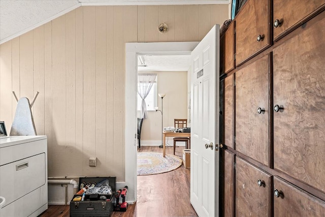 clothes washing area with washer / dryer, cabinet space, wood walls, and dark wood-style floors