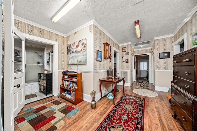 interior space with wallpapered walls, ornamental molding, a textured ceiling, and wood finished floors