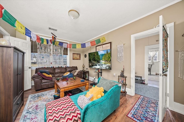 living room with visible vents, baseboards, wood finished floors, a textured ceiling, and crown molding