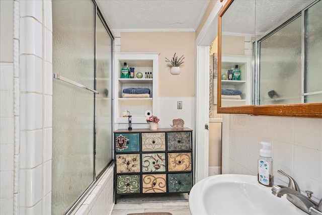 full bathroom with an enclosed shower, a textured ceiling, tile walls, and a sink