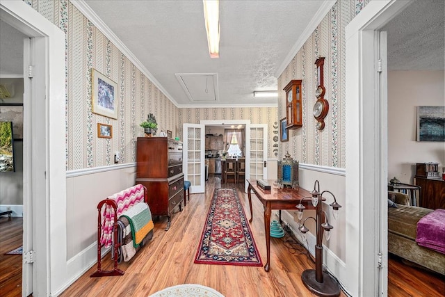 hallway featuring attic access, wood finished floors, a textured ceiling, and wallpapered walls