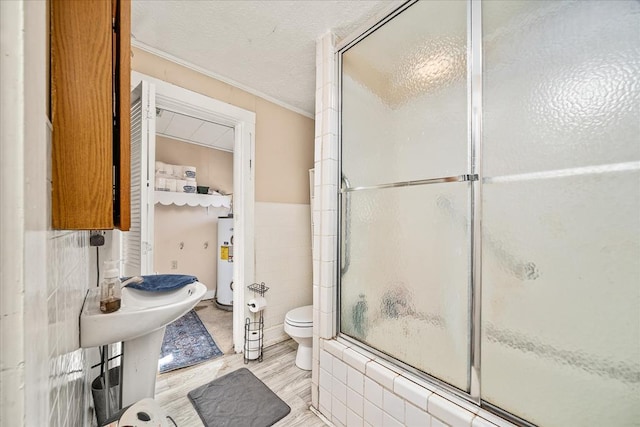 bathroom featuring tile walls, water heater, toilet, an enclosed shower, and a textured ceiling