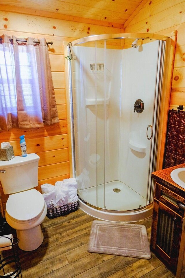 bathroom with a stall shower, wood finished floors, vanity, and wooden walls