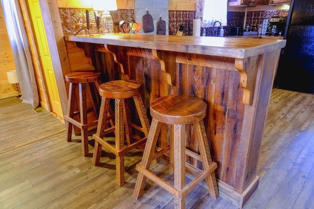 bar featuring light wood-type flooring, freestanding refrigerator, and a bar