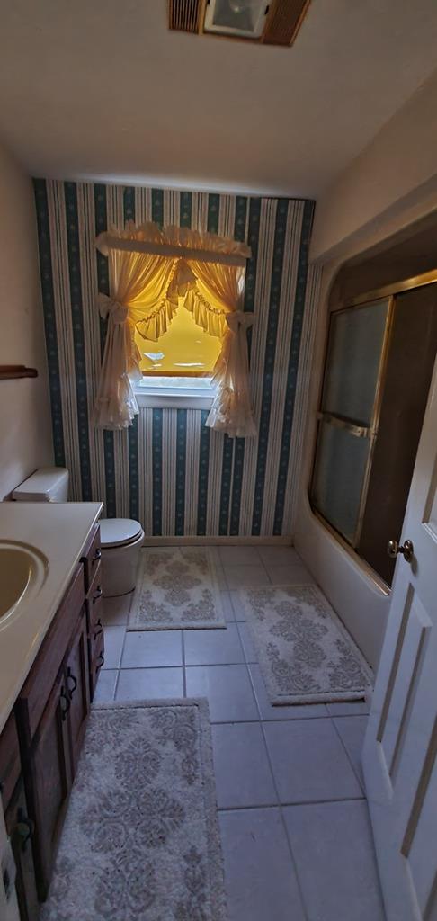 bathroom with toilet, vanity, combined bath / shower with glass door, tile patterned floors, and wallpapered walls