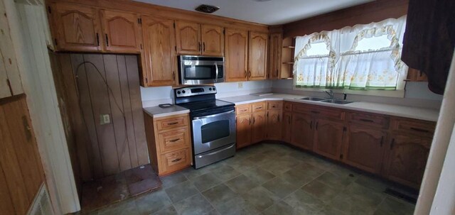 kitchen featuring light countertops, appliances with stainless steel finishes, brown cabinetry, and a sink