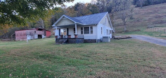 view of front facade with central air condition unit, a porch, metal roof, an outdoor structure, and a front lawn