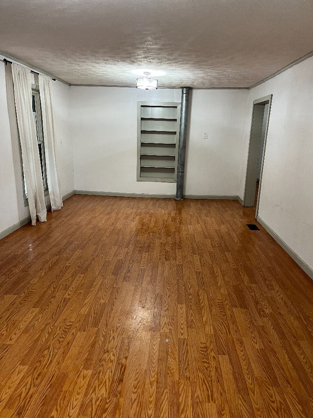 empty room with a textured ceiling, wood finished floors, and baseboards