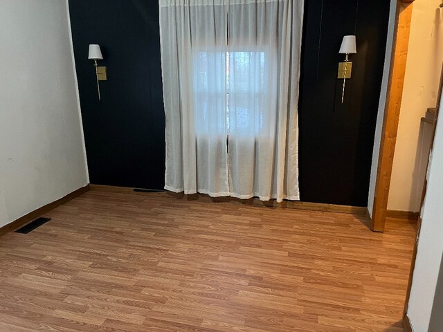 empty room with light wood finished floors, visible vents, and baseboards