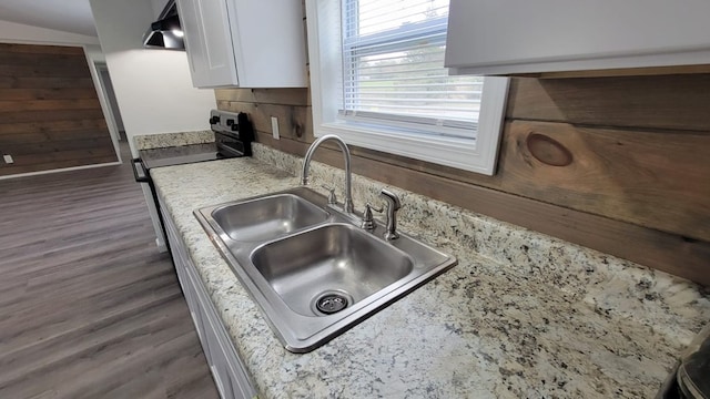 kitchen with under cabinet range hood, range with electric stovetop, a sink, white cabinets, and dark wood finished floors