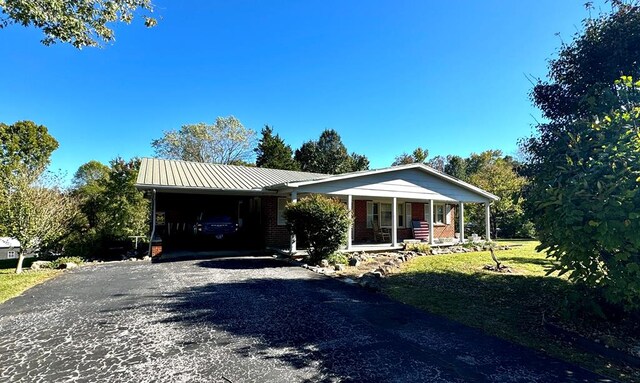 ranch-style home with metal roof, an attached carport, gravel driveway, covered porch, and brick siding