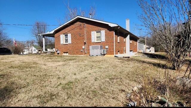 rear view of property featuring brick siding, a yard, and a chimney