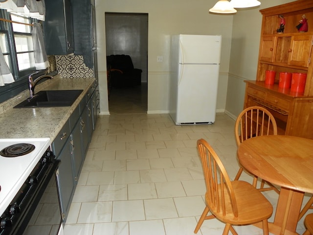 kitchen featuring light stone counters, decorative backsplash, freestanding refrigerator, a sink, and range with electric cooktop