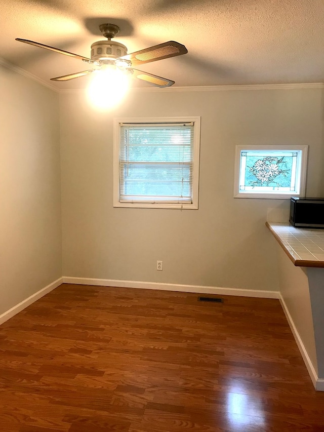 spare room featuring a textured ceiling, dark wood-type flooring, visible vents, baseboards, and crown molding