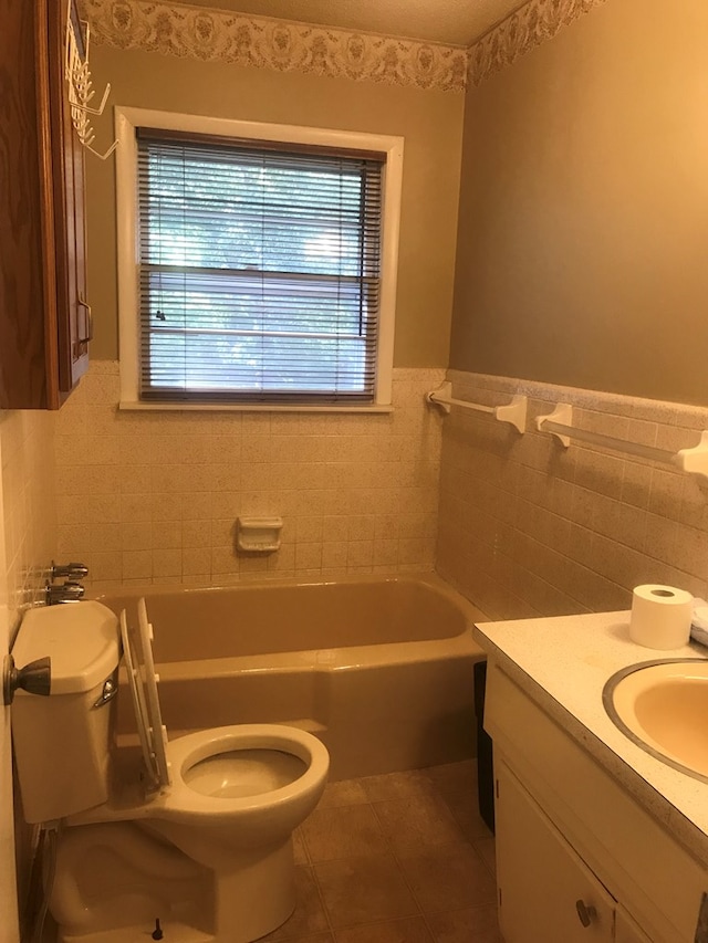 bathroom with toilet, a bathing tub, tile patterned flooring, vanity, and tile walls