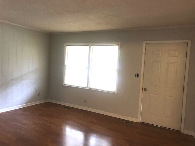 spare room featuring dark wood-style flooring, visible vents, crown molding, and baseboards