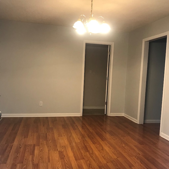 empty room featuring dark wood-style floors, baseboards, and an inviting chandelier