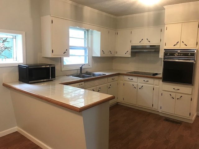 kitchen with tile countertops, black appliances, under cabinet range hood, and white cabinets