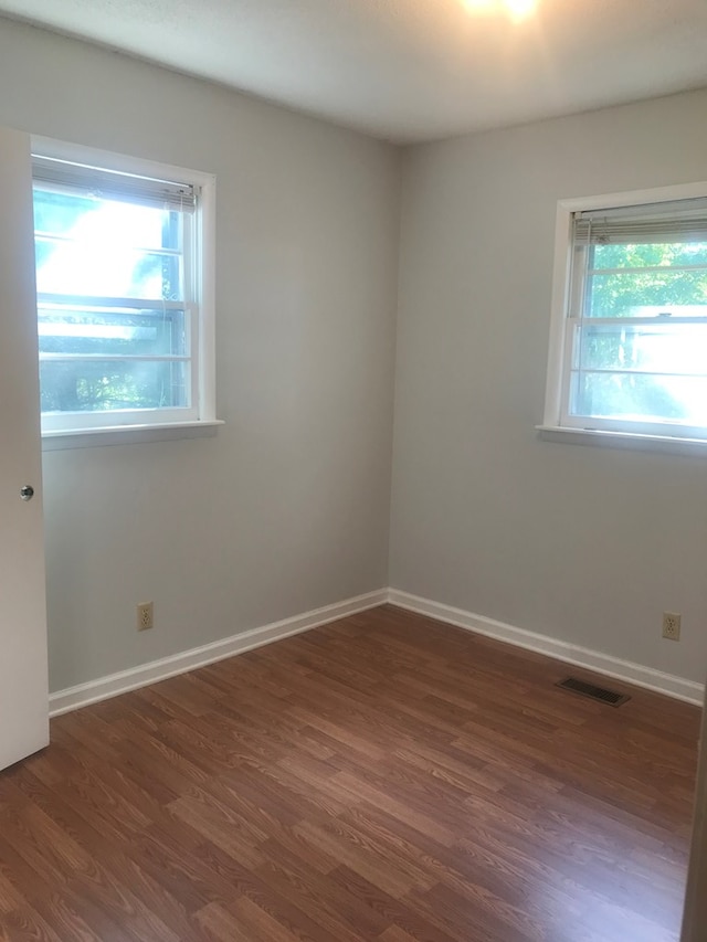 empty room featuring dark wood-style flooring, visible vents, and baseboards